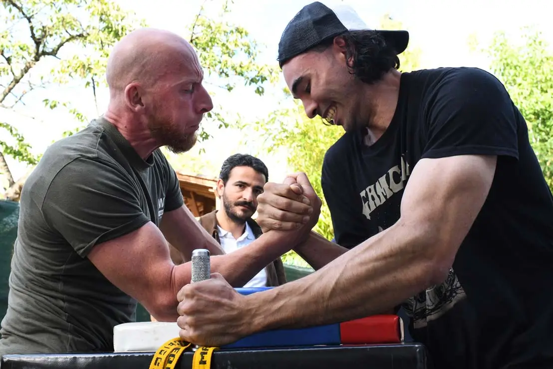 Deux athlètes s’affrontent lors d’un duel de bras de fer sportif au club X-MEN Armwrestling à Paris, sous le regard d’un arbitre.